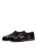 Side angle of black slip-on sneakers featuring colorful tattoo frogs and bold anti-tattoo slogan on canvas