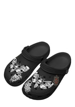Angled view of black slip-ons featuring skull moths and floral tattoo graphics
